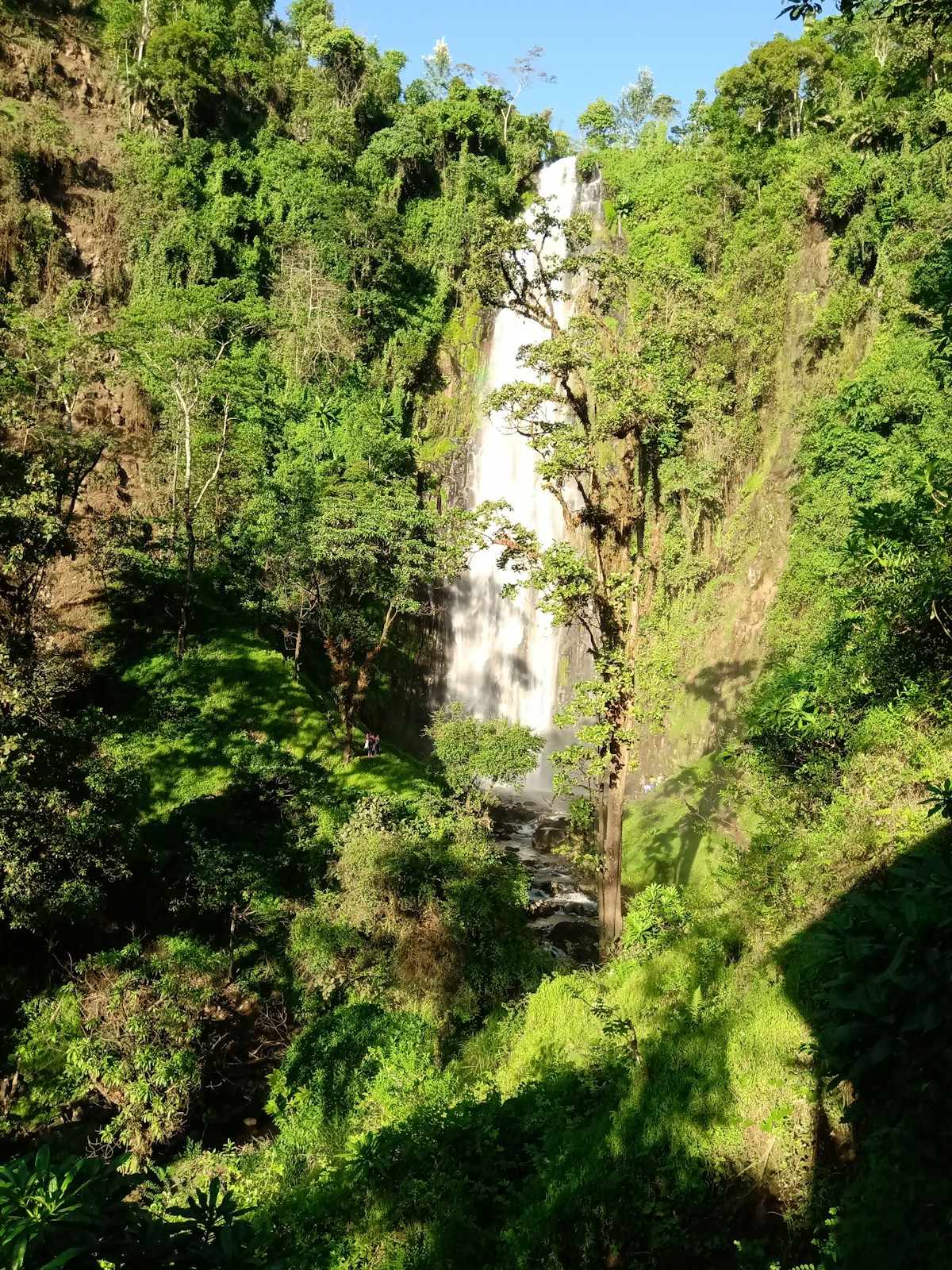 Hikers trekking toward Materuni Waterfall through lush green hills