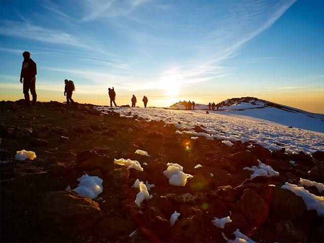 Trekkers crossing snowy volcanic terrain on Mount Kilimanjaro at sunrise